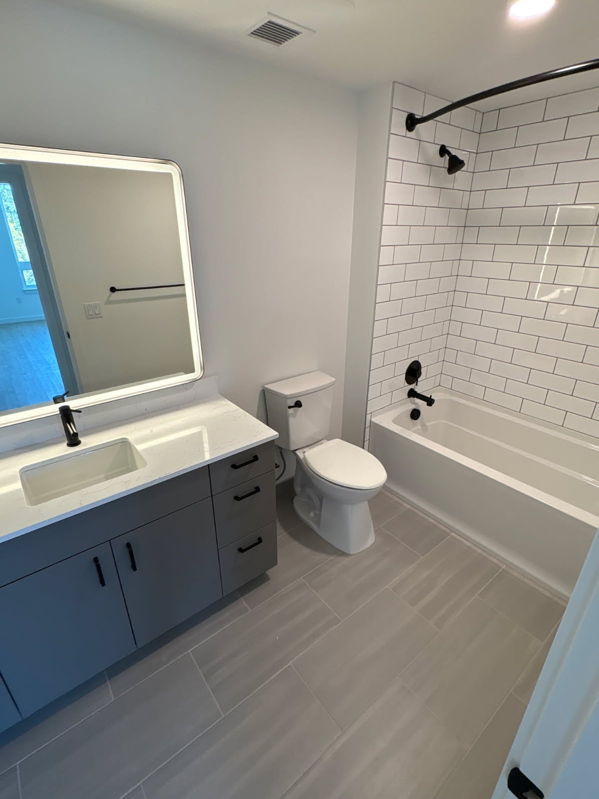 Completed bathroom remodel — subway-tile tub surround, quartz vanity, matte black fixtures