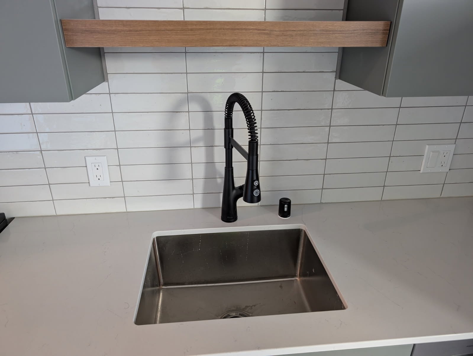 Commercial-style matte black spring faucet over stainless sink with white tile backsplash